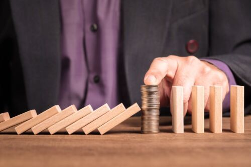 Businessman place the money heap in a row of wooden domino that continuously falling down to stop the crash